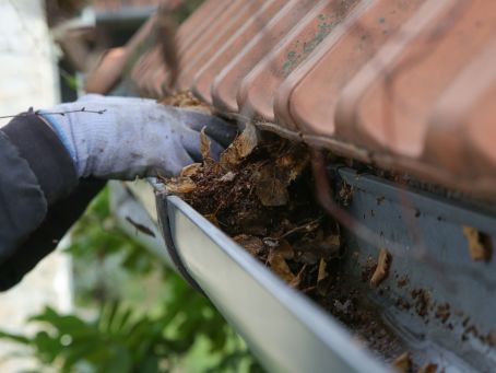A close up shot of a man cleaning a gutter on the side of a roof
