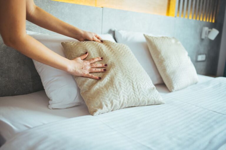 A woman plumping up her cushion on her bed after cleaning it