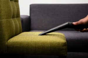 a green chair being cleaned and vacuumed in a living room with a sofa in the background