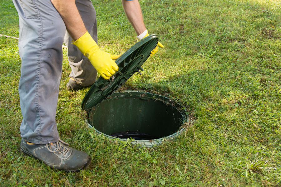 a man wearing yellow gloves lifting a drain lid on a patch of land
