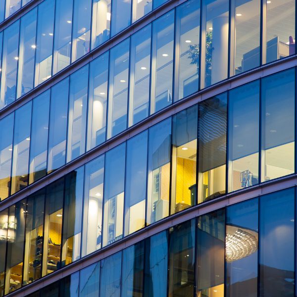 Modern office and corporate building exterior with glass facade and illuminated workspaces